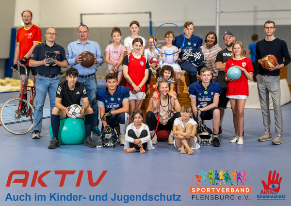 Zeigt Gruppe von Menschen unterschiedlichen Alters mit verschiedenen Sportgeräten in einer Sporthalle stehend.