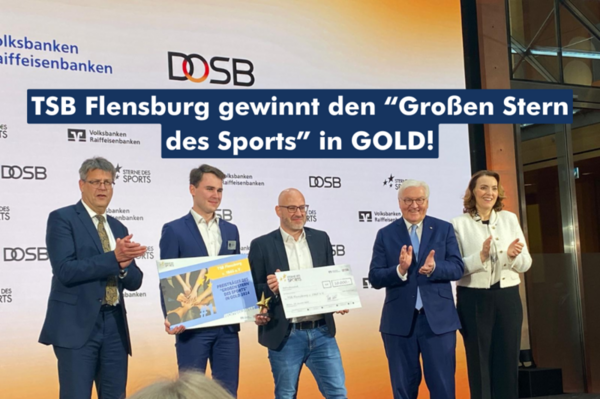 Vier Personen in Anzügen gekleidet präsentieren den Gewinn auf einer Bühne stehend.